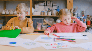 Two young children drawing and coloring at a classroom table