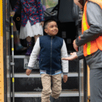 Boy stepping off a school bus with help from an adult