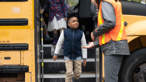 Boy stepping off a school bus with help from an adult