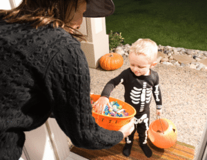 Toddler in a skeleton costume trick-or-treating with an adult