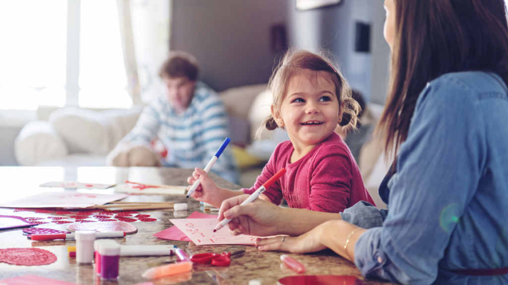 Children making Valentine's crafts at a table with a parent