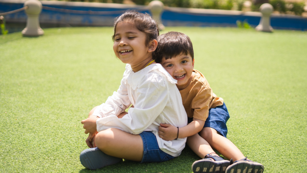 Two smiling children hugging while sitting on the grass