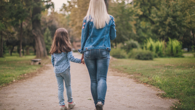 Mother and daughter walking hand in hand down a park path