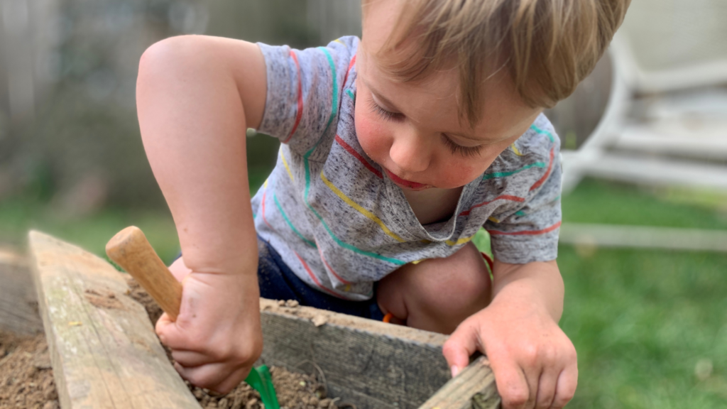 Toddler digging in a garden bed with a small shovel