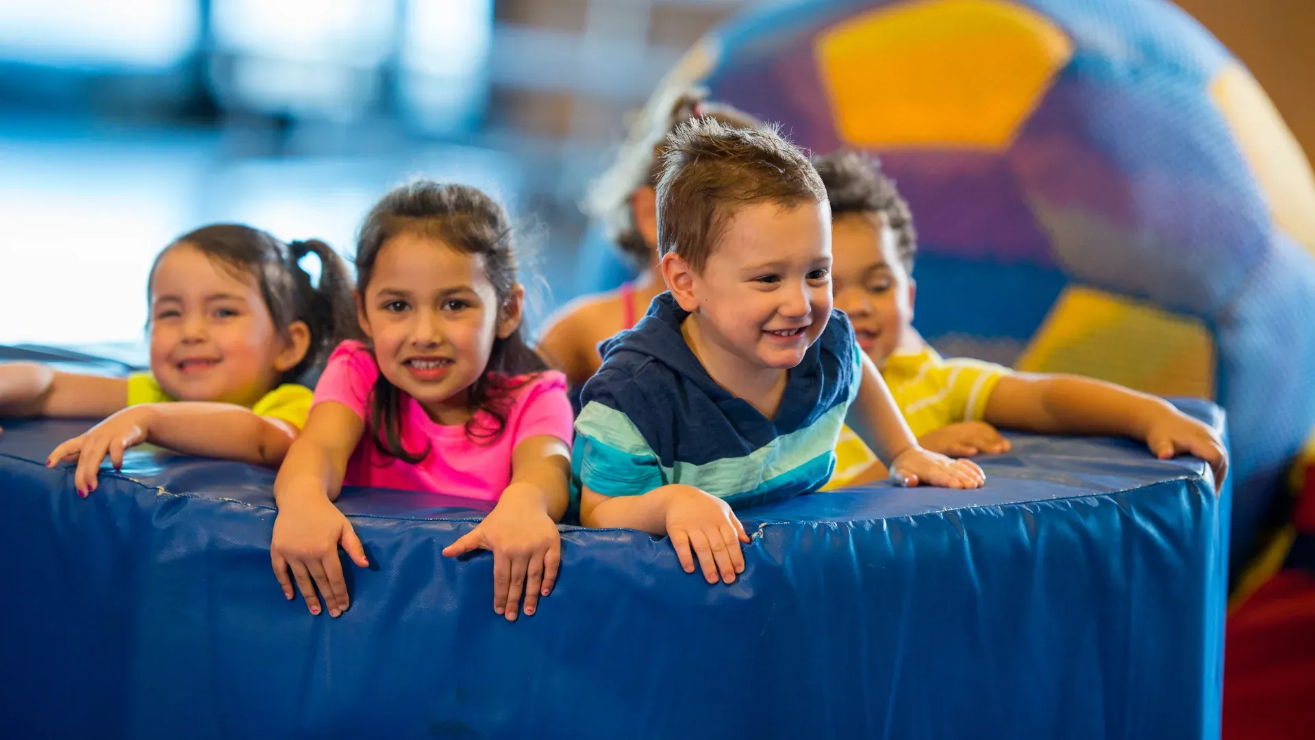 Smiling children leaning on a blue gym mat during a social skills group