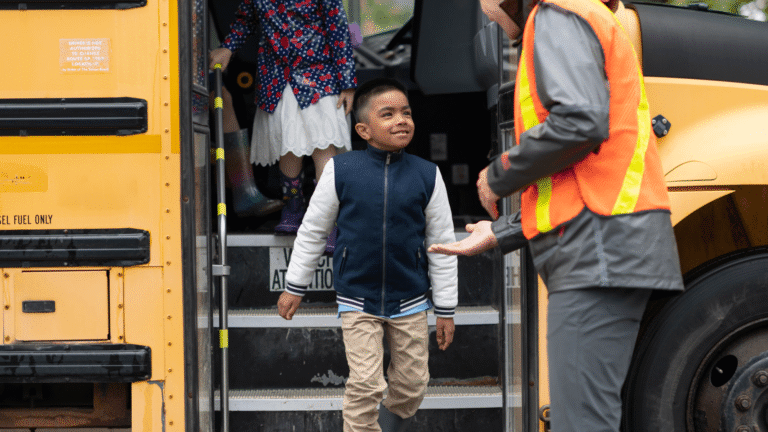 Boy stepping off a school bus with help from an adult
