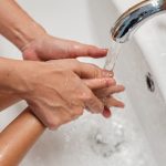 Parent guiding a young child’s hands under the faucet while washing hands at a bathroom sink